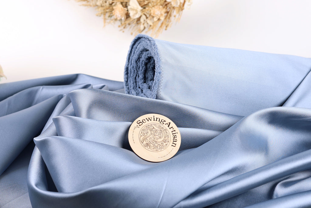 A blue satin fabric with a wooden sewing machine logo in the center, placed on top of it.
