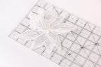 A white sequin flower is placed on a clear ruler with measurement markings.