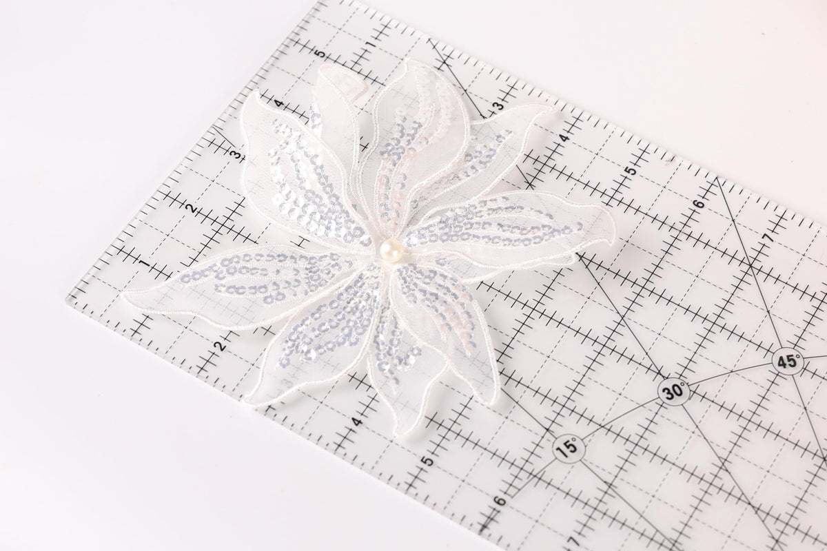 A white sequin flower is placed on a clear ruler with measurement markings.