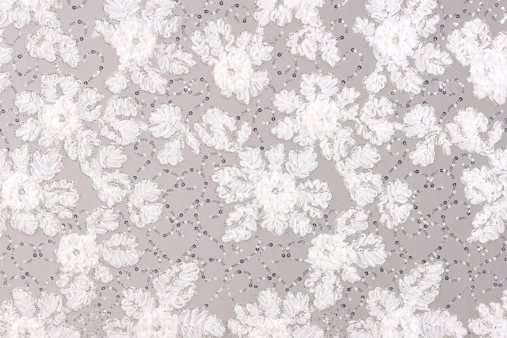 The image is a close-up of a fabric with a floral pattern, featuring white flowers and small beads or sequins scattered throughout the fabric.