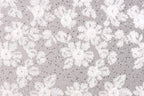 The image is a close-up of a fabric with a floral pattern, featuring white flowers and small beads or sequins scattered throughout the fabric.