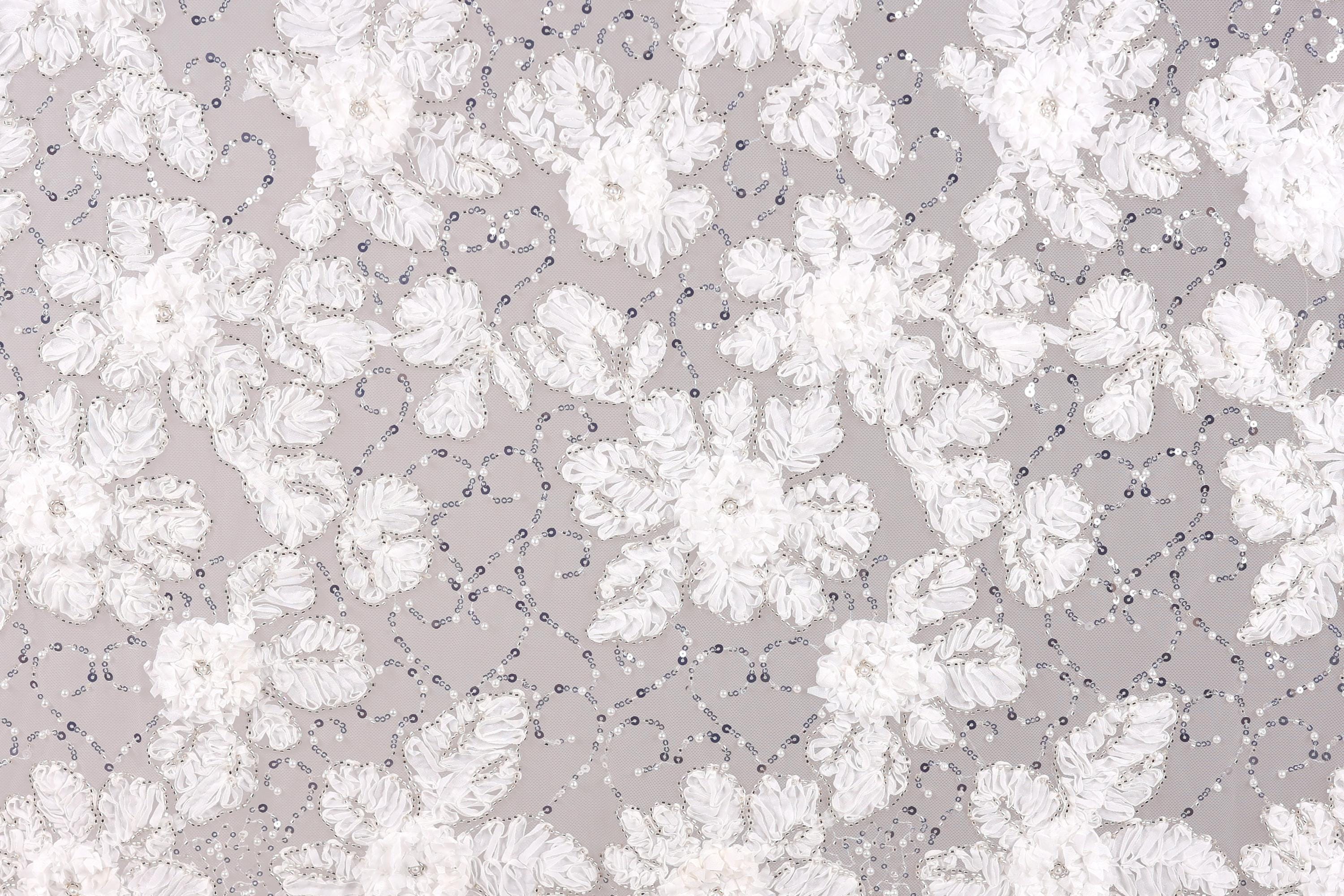 The image is a close-up of a fabric with a floral pattern, featuring white flowers and small beads or sequins scattered throughout the fabric.