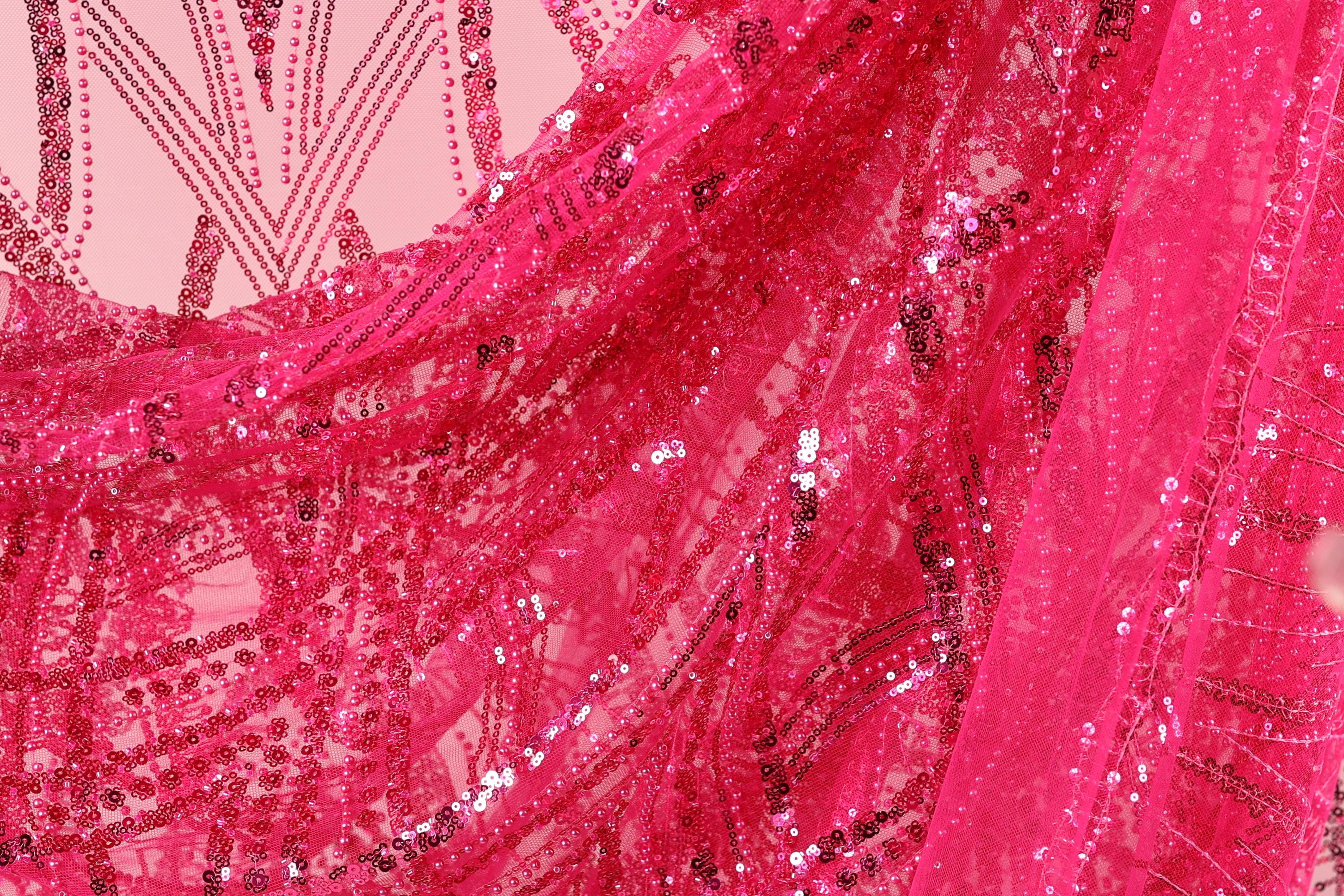 The image is a close-up of a vibrant pink fabric with a pattern of sequins and beads, creating a visually striking and eye-catching design.