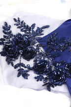 a close-up view of a fabric with a floral pattern, including blue sequin flowers and leaves. The fabric appears to be a light blue color, and the intricate details of the floral design are clearly visible.