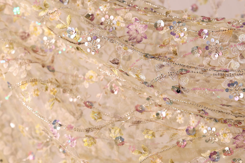 The image is a close-up of a delicate, intricately embroidered fabric with a floral pattern. The fabric appears to be made of sheer material, giving it a soft and delicate appearance. The embroidery features a variety of flowers and leaves, creating a visually appealing and intricate design. The colors used in the embroidery are predominantly pink, yellow, and green, adding to the overall beauty of the fabric.