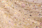 The image is a close-up of a delicate, intricately embroidered fabric with a floral pattern. The fabric appears to be made of sheer material, giving it a soft and delicate appearance. The embroidery features a variety of flowers and leaves, creating a visually appealing and intricate design. The colors used in the embroidery are predominantly pink, yellow, and green, adding to the overall beauty of the fabric.