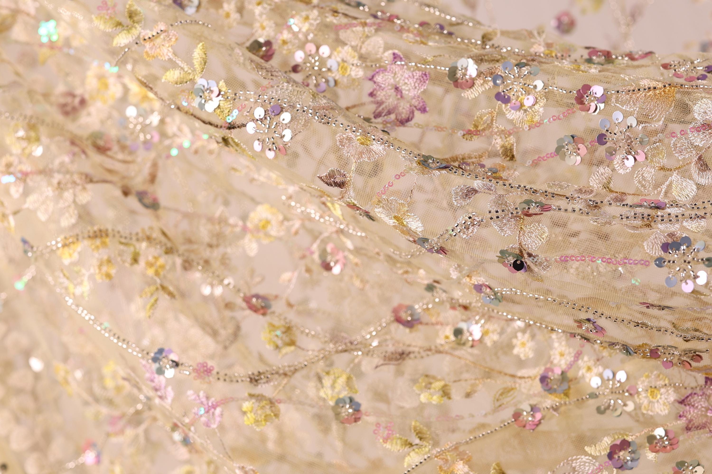 The image is a close-up of a delicate, intricately embroidered fabric with a floral pattern. The fabric appears to be made of sheer material, giving it a soft and delicate appearance. The embroidery features a variety of flowers and leaves, creating a visually appealing and intricate design. The colors used in the embroidery are predominantly pink, yellow, and green, adding to the overall beauty of the fabric.
