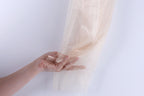 A hand is holding a piece of beige, shimmering fabric against a white background.