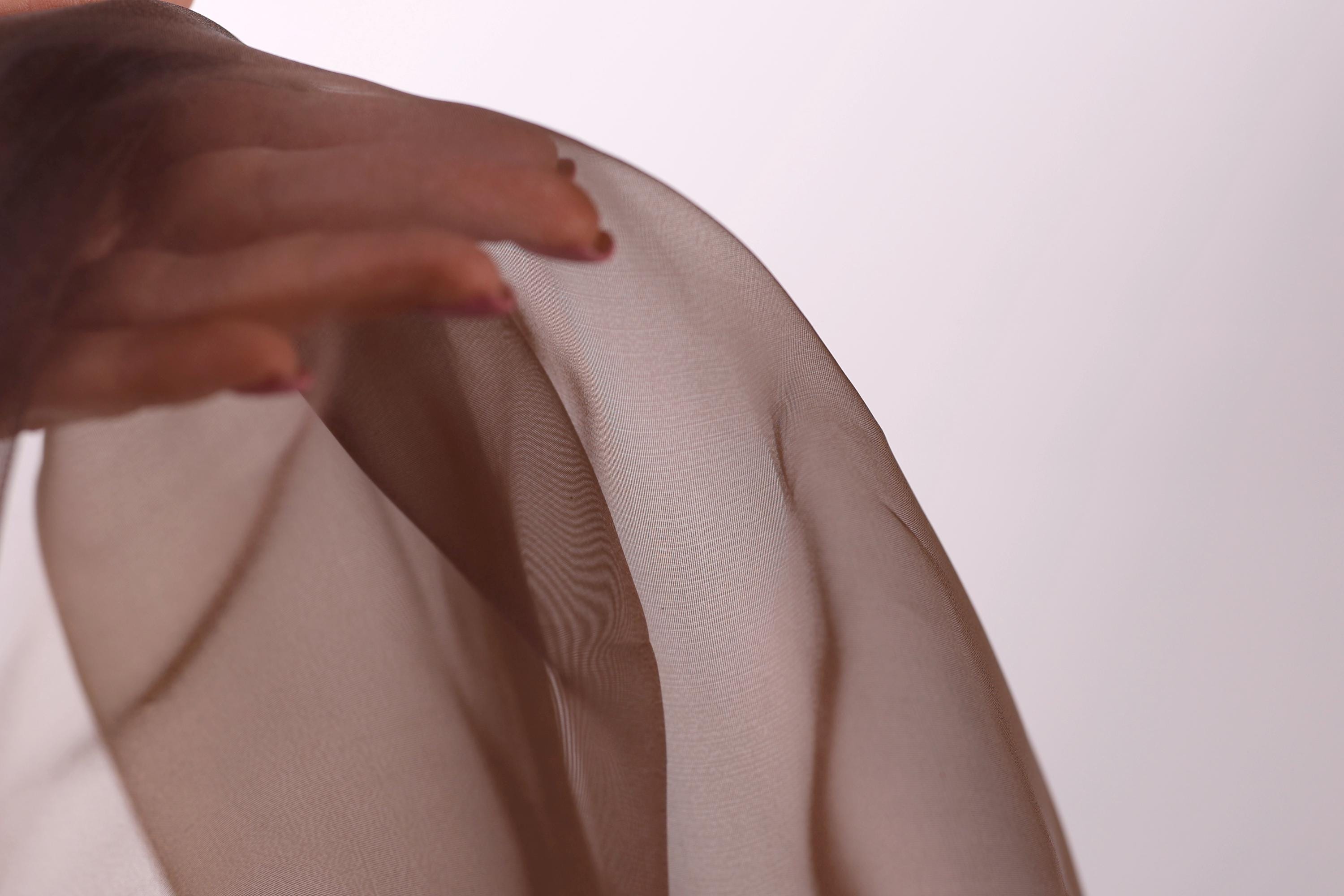 A close-up view of a hand gently touching a piece of sheer, light brown fabric.