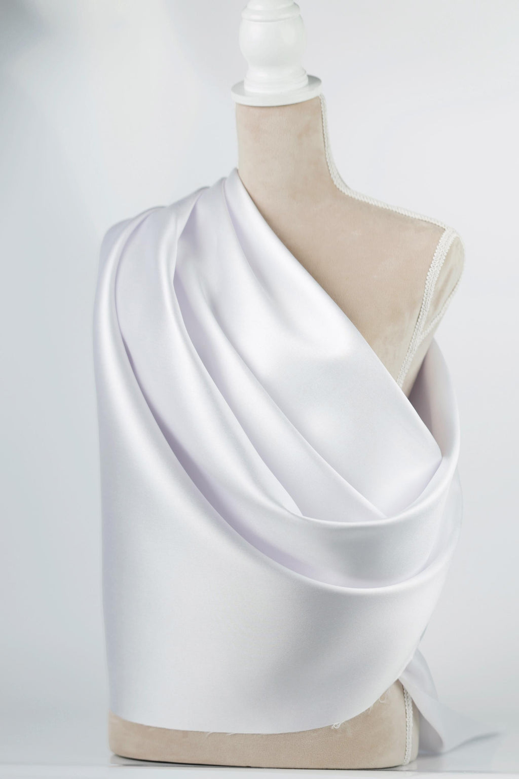 A mannequin wearing a white satin fabric draped over its body.