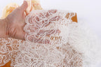 A hand is holding a piece of delicate white lace against a plain white background.
