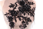 a close-up view of a delicate, intricate black lace design with a floral pattern. The lace appears to be made of sheer fabric, giving it a delicate and elegant appearance. The design features a variety of black flowers and leaves, which are intricately sewn onto the fabric, creating a visually striking and detailed piece of textile art.