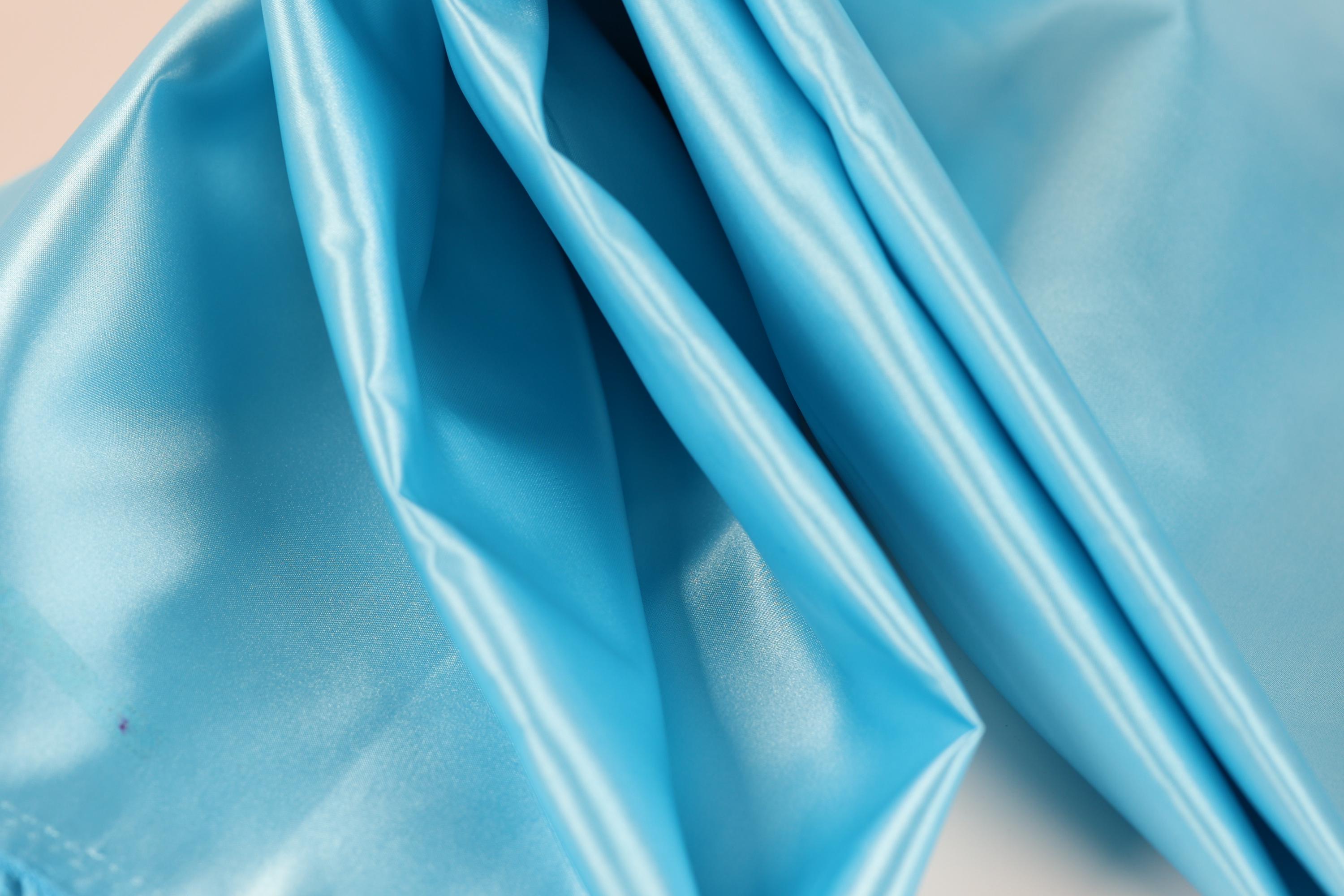 The image is a close-up of a blue satin fabric, with its folds and creases clearly visible.