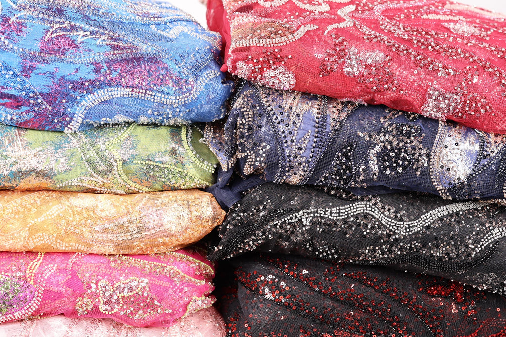 A close-up image of colorful, patterned fabric with sequins and beads, stacked on top of each other.
