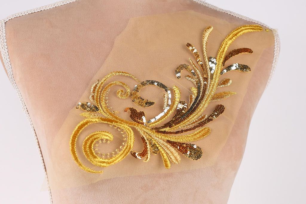 a close-up view of a delicate gold and beige embroidered design on a fabric, showcasing intricate patterns and details.
