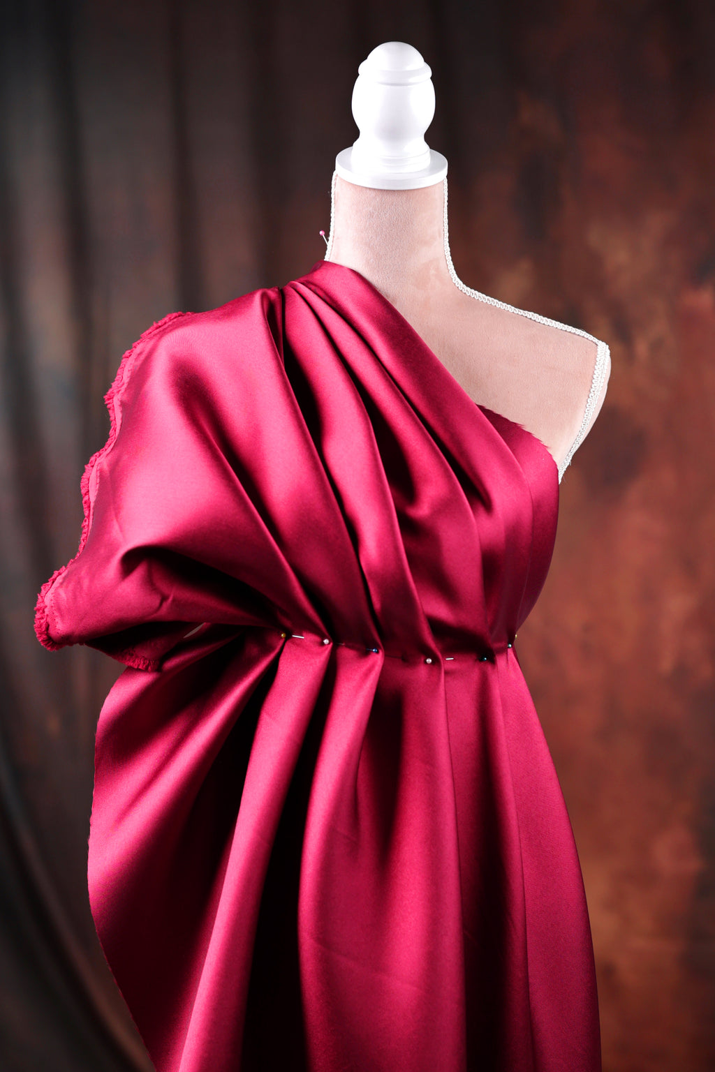 A mannequin wearing a vibrant red one-shoulder dress with a draped, flowing skirt.