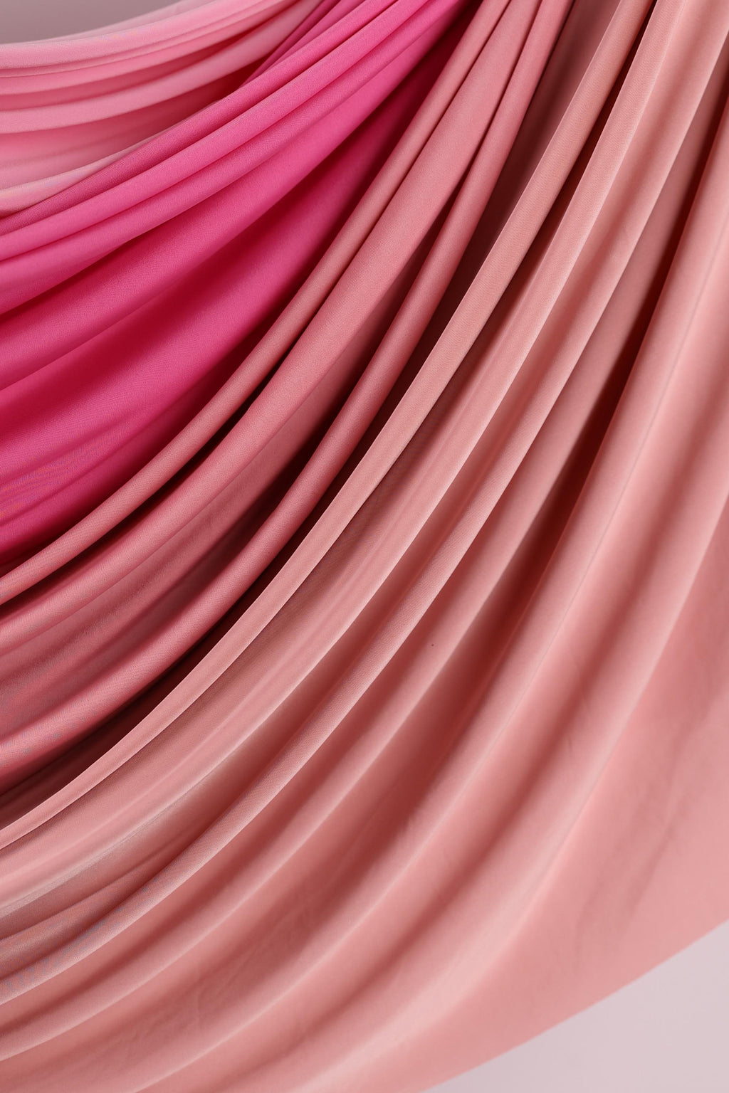 a close-up view of a fabric with a soft, flowing texture in shades of pink and red. The fabric appears to be made of a soft, plush material, possibly cotton or silk, and is arranged in a way that creates a sense of movement and depth. The colors are vibrant and the fabric's texture is smooth, giving the image a visually appealing and artistic appearance.
