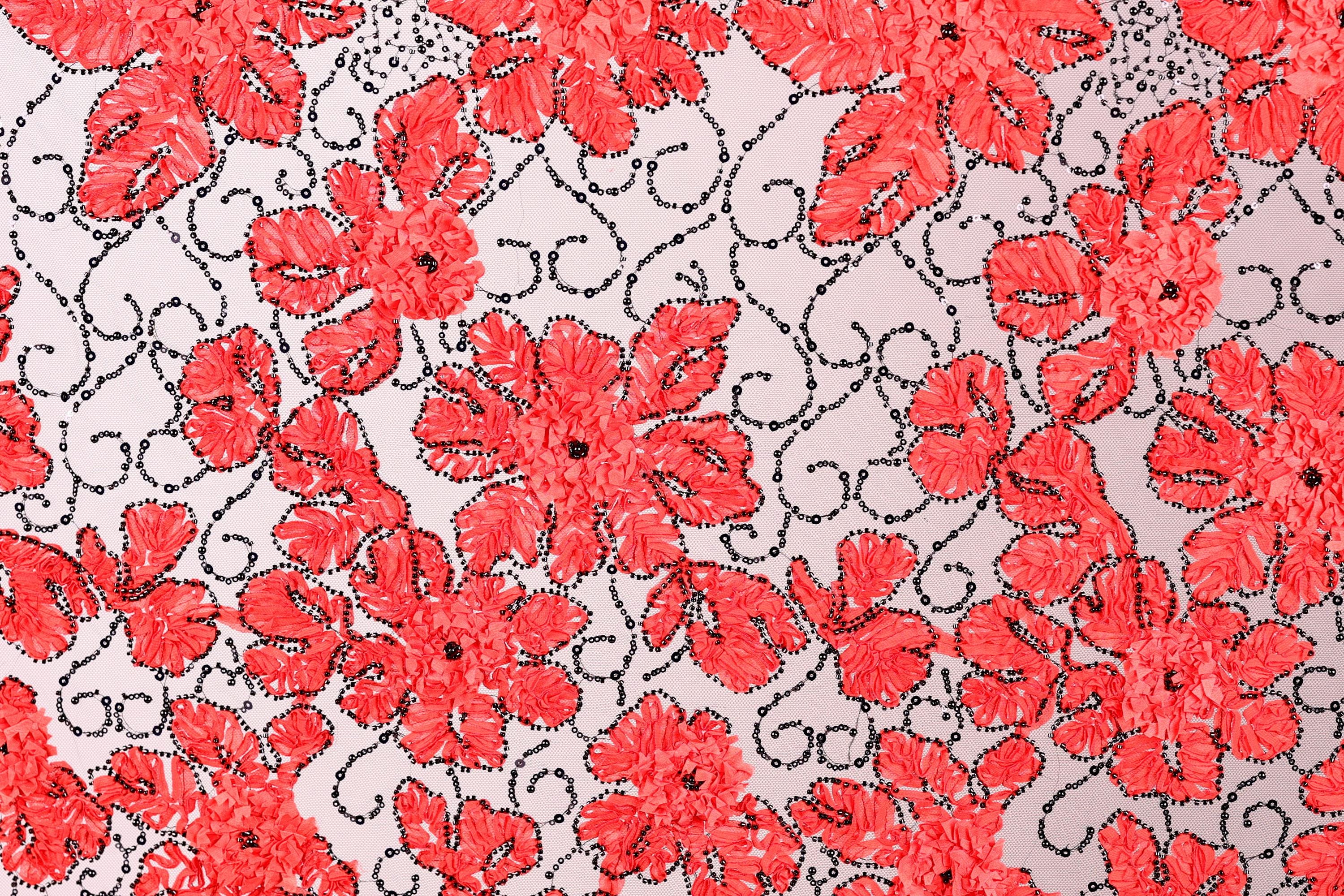 a close-up view of a fabric with a repeating pattern of red flowers against a light background. The flowers are intricately designed and appear to be made of a shiny material, giving them a sparkling appearance. The pattern is composed of numerous small red flowers arranged in a visually striking manner, creating a vibrant and eye-catching design.