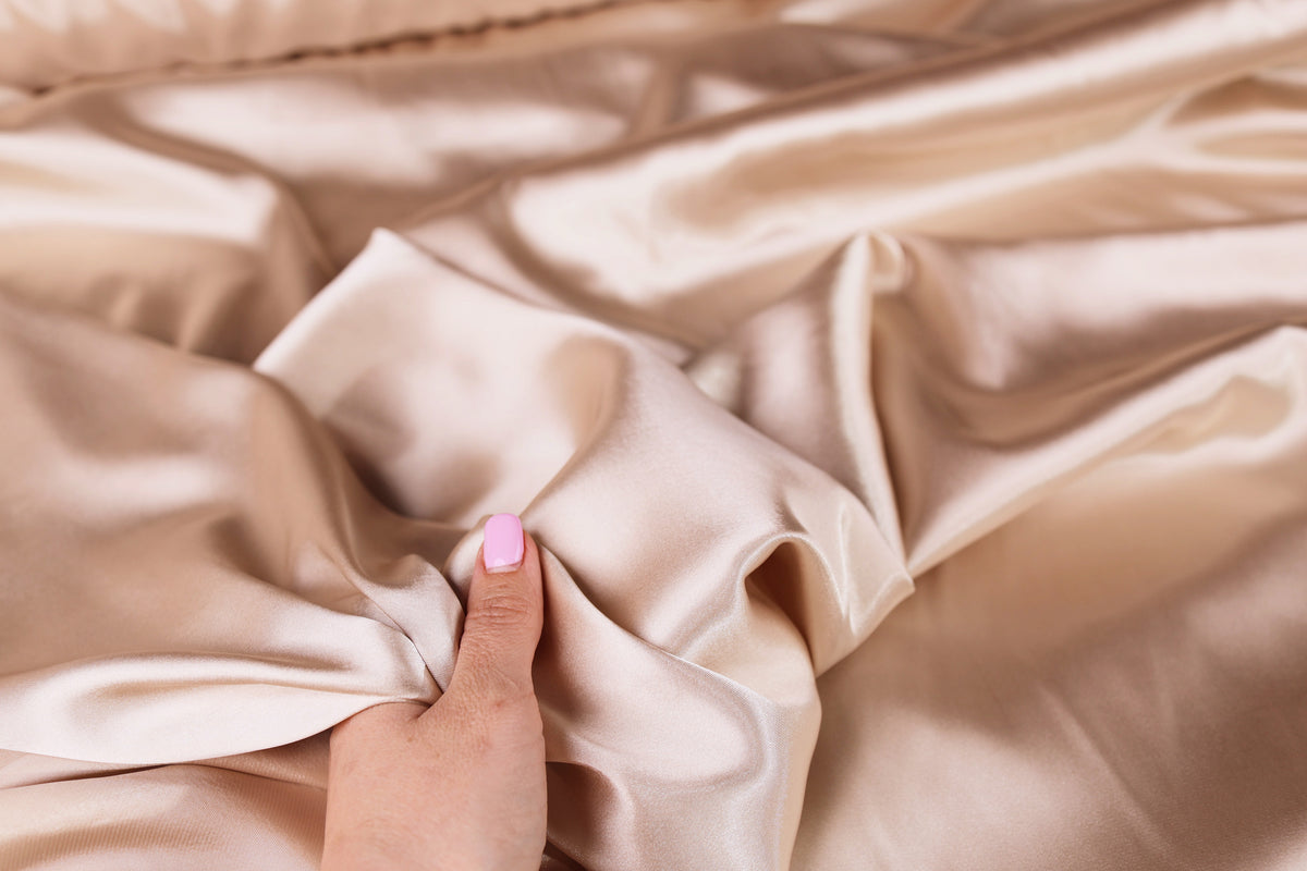 A hand with pink nail polish is holding a piece of crumpled beige fabric.