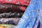A close-up image of various colorful and patterned fabric swatches, including red, black, blue, and silver sequin designs.