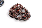 A close-up image of a decorative piece with a black background and a pattern of red and brown gemstones.