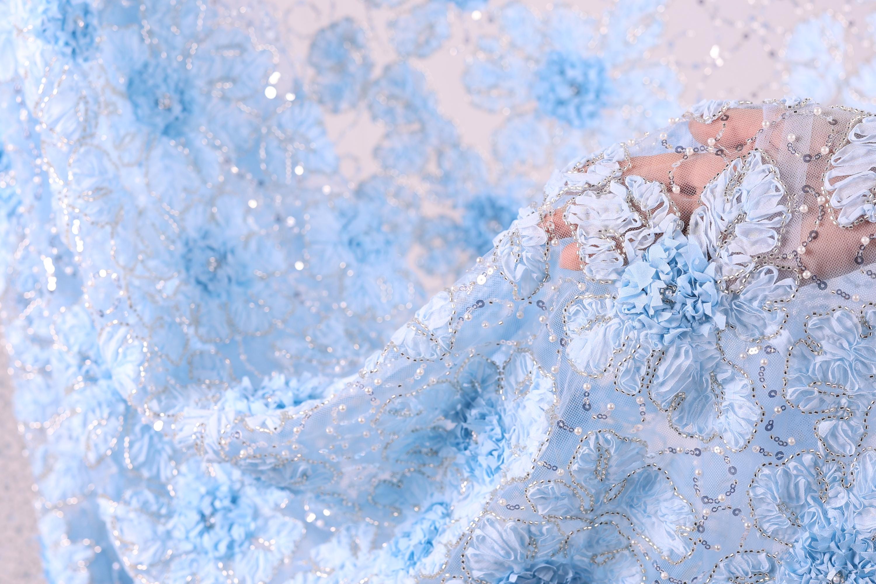 A close-up view of a delicate, intricately designed fabric with a floral pattern in shades of blue and white.
