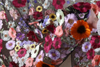 The image is a close-up view of a fabric with a vibrant floral pattern, featuring a variety of colorful flowers such as red, orange, yellow, and purple.