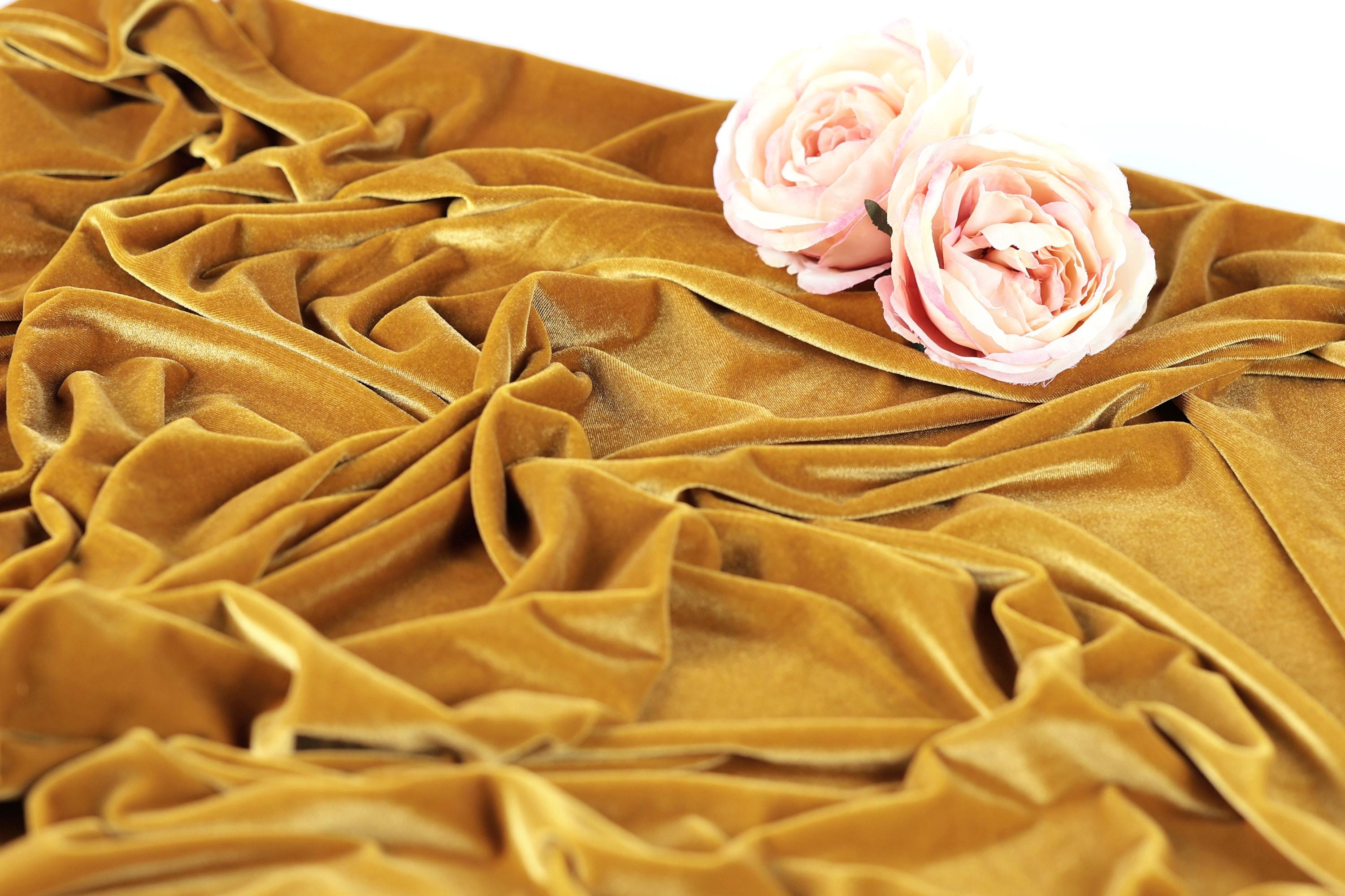 a close-up view of a crumpled, golden fabric with two delicate pink roses resting on top of it.