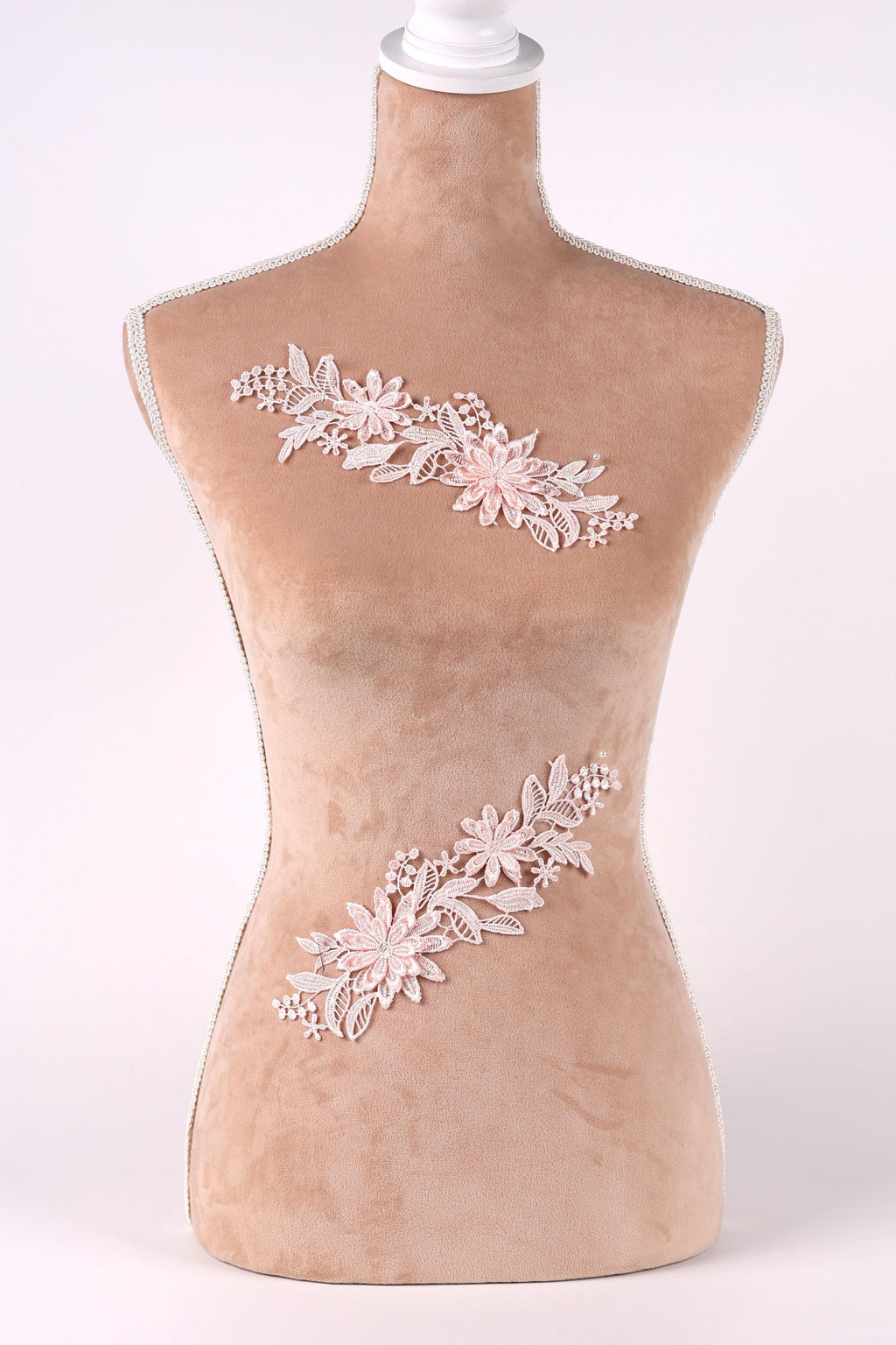 A mannequin with a beige body and a white head, wearing a floral embroidered piece of clothing.
