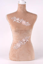 A mannequin with a beige body and a white head, wearing a floral embroidered piece of clothing.