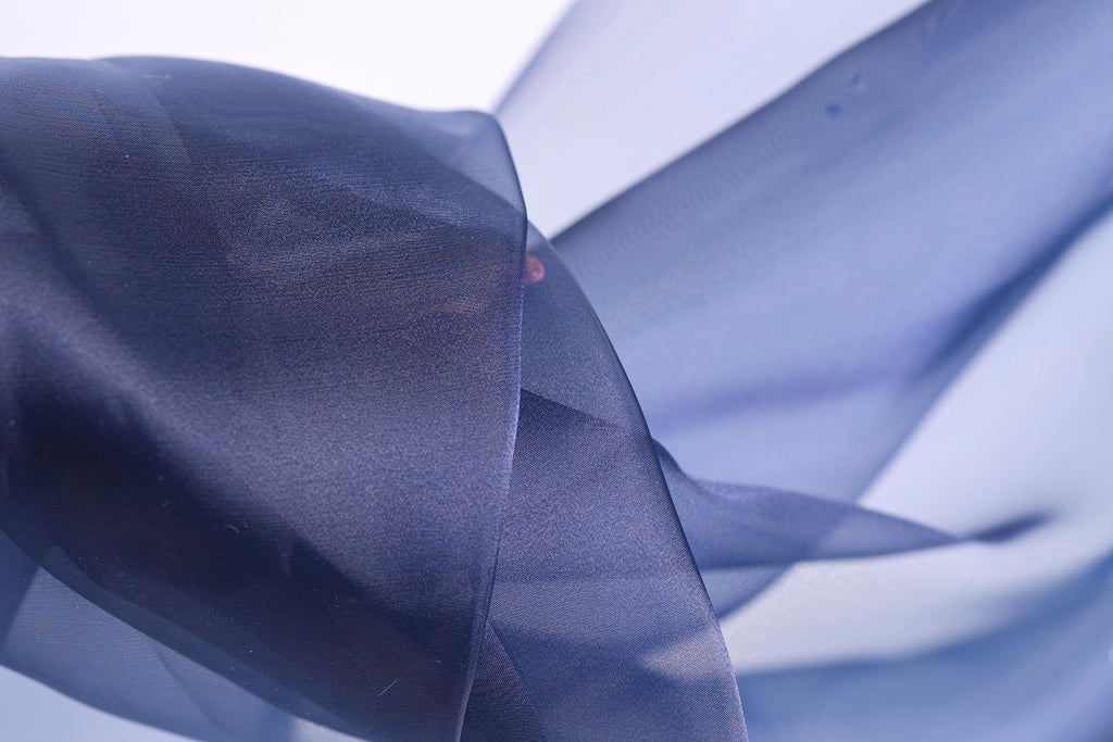 The image is a close-up of a blue fabric, possibly silk or chiffon, with a blurred background.