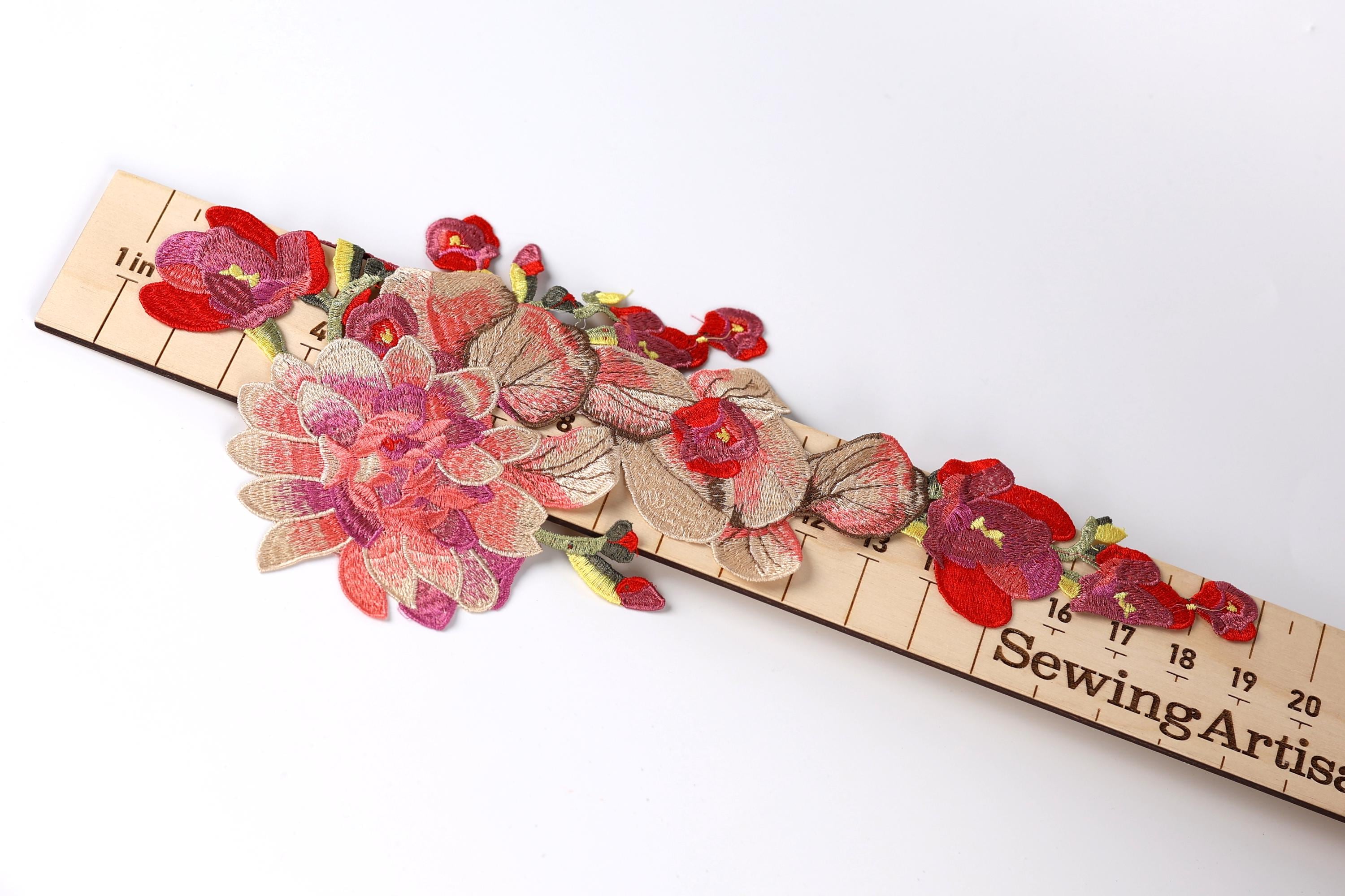 A wooden ruler with a floral embroidery design on it, featuring red and pink flowers and leaves.