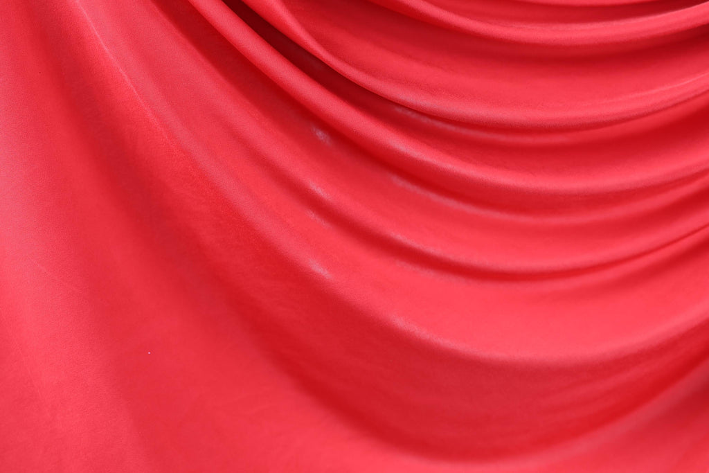 The image is a close-up of a red fabric, possibly silk or chiffon, with a smooth, flowing texture.
