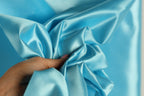 A hand is holding a piece of blue satin fabric, which appears to be a close-up view of the material.