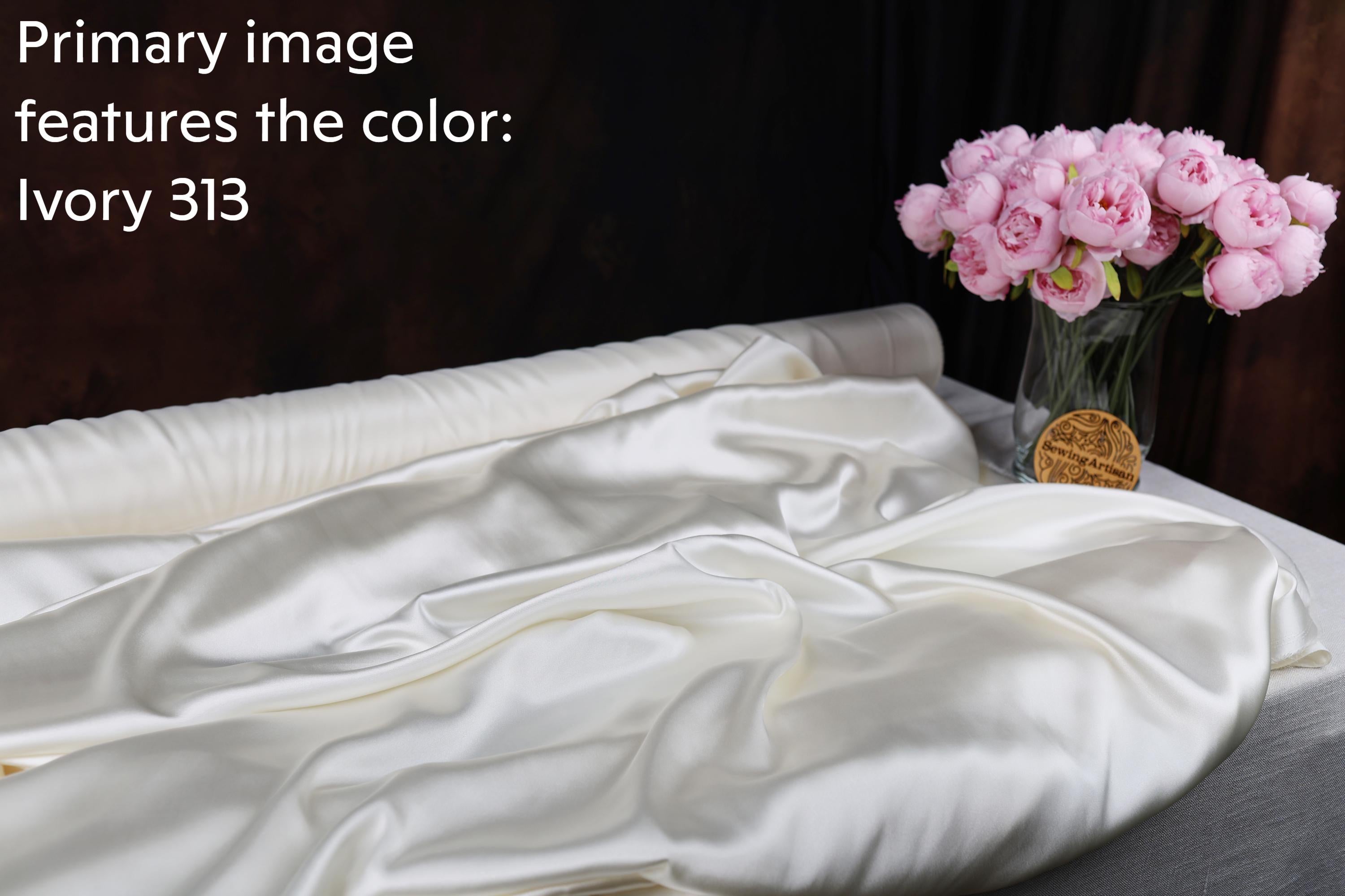 a white satin fabric with a vase of pink peonies on a table.