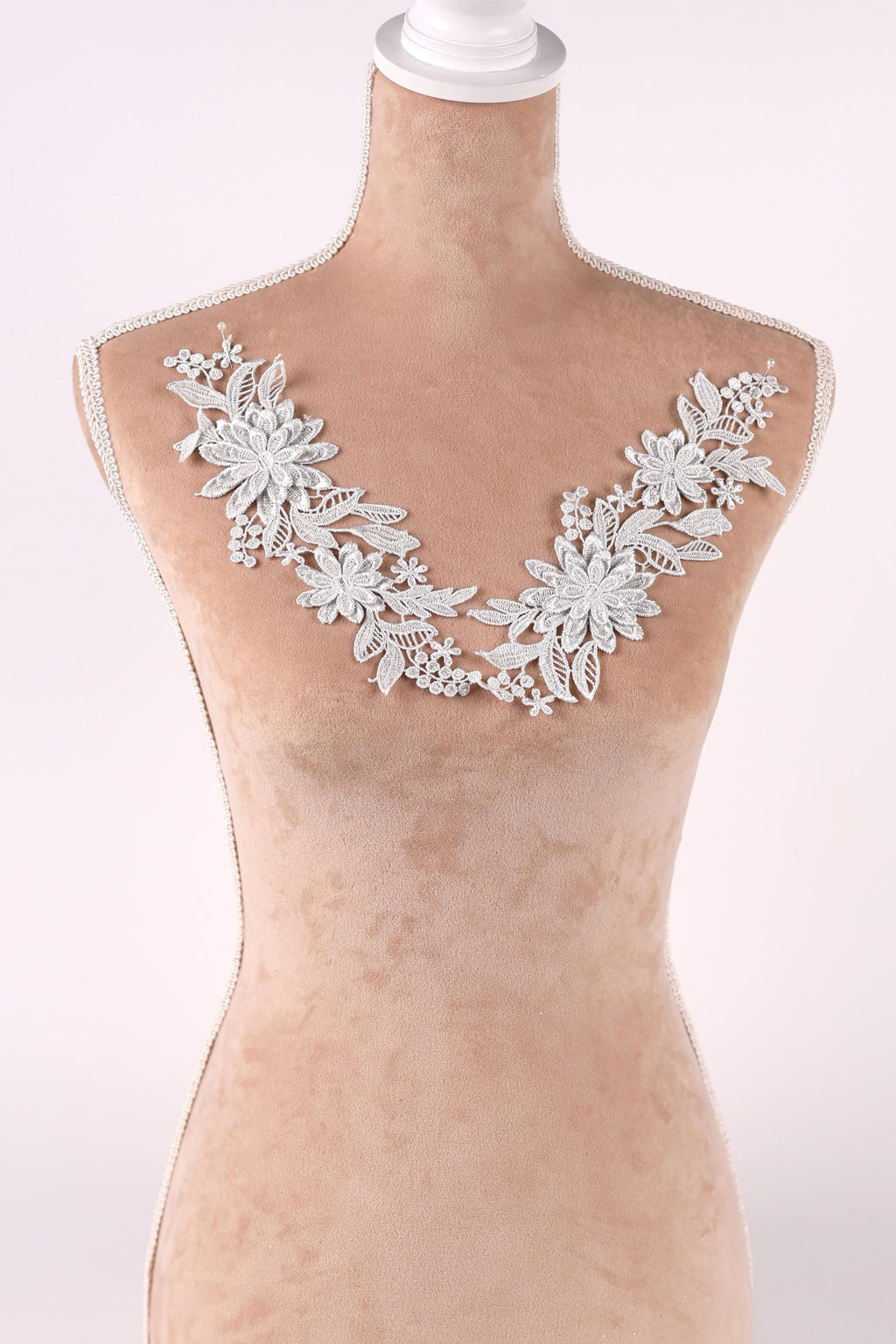 A mannequin wearing a white lace collar with delicate floral designs.