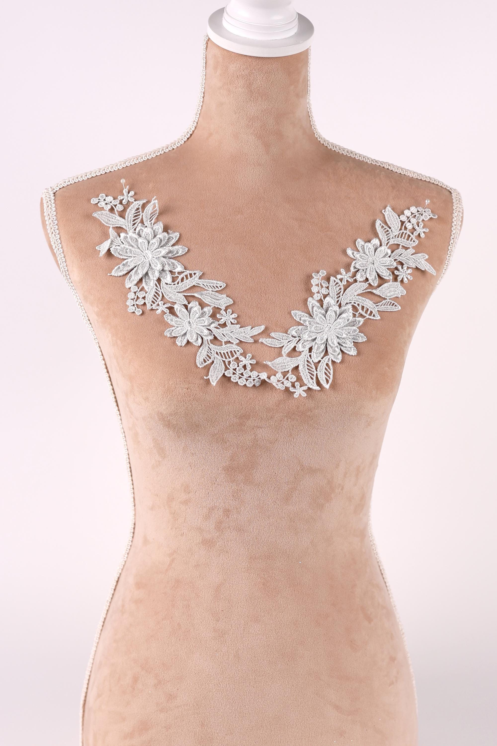 A mannequin wearing a white lace collar with delicate floral designs.
