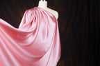 A mannequin wearing a flowing, one-shoulder pink satin dress against a dark background.