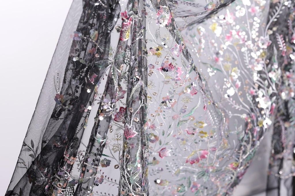 a close-up view of a delicate, intricately embroidered fabric with a floral pattern. The fabric appears to be a sheer material, with a black background that contrasts with the colorful floral design. The image is not a single, continuous scene but rather a close-up of a section of the fabric, showcasing the detailed embroidery and the intricate design.