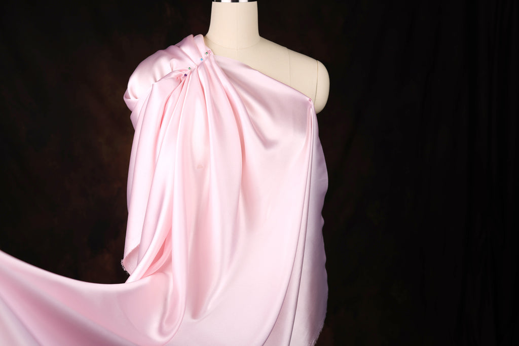 A mannequin wearing a pink satin one-shoulder dress with a flowing, draped design.