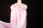 A mannequin wearing a pink satin one-shoulder dress with a flowing, draped design.