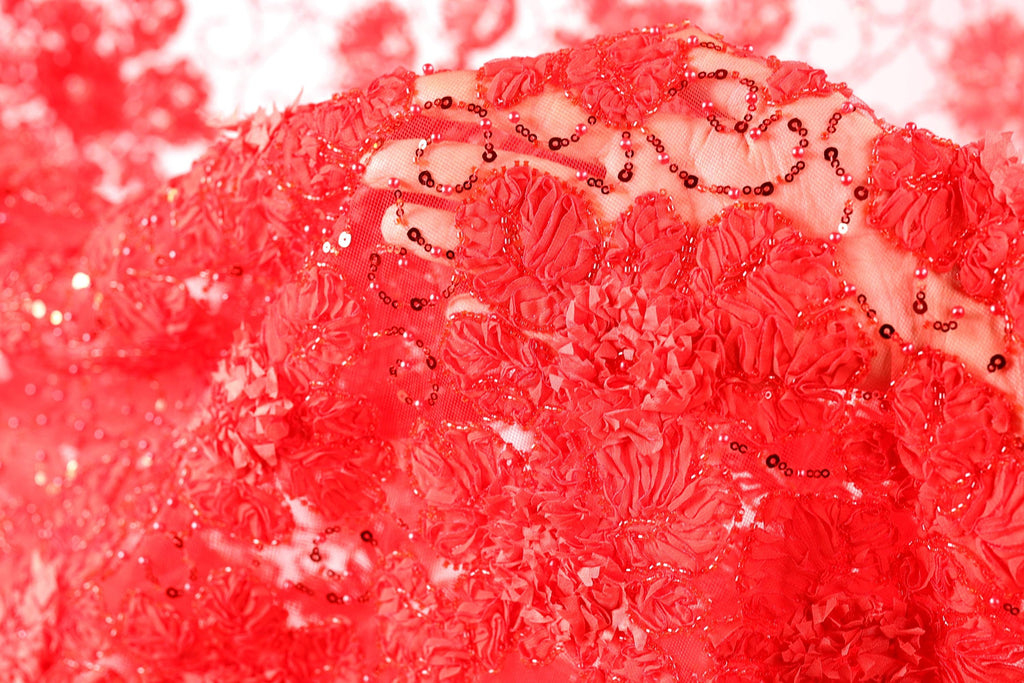 The image is a close-up of a vibrant red fabric with a floral pattern, adorned with small red beads or sequins.