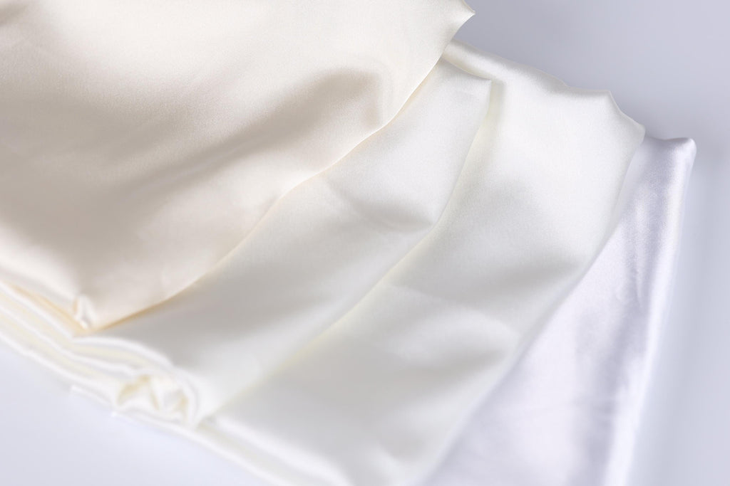 a close-up view of a white fabric, possibly silk or satin, with a subtle texture and a soft, shiny appearance.