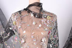 a close-up view of a sheer, black fabric with a floral pattern. The fabric appears to be made of sheer material, giving it a delicate and airy appearance. The floral pattern consists of various flowers and leaves, creating a visually appealing and intricate design. The fabric is displayed on a mannequin, which is positioned in the center of the image. The background of the image is white, which contrasts with the black fabric and allows the details of the floral pattern to stand out.