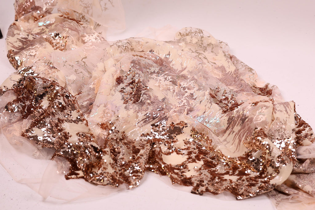 a close-up view of a fabric with a metallic, glittery texture. The fabric appears to be a blend of white and gold colors, with a metallic sheen that adds a touch of sparkle to the overall appearance. The fabric is spread out on a white surface, creating a visually striking contrast with the background.