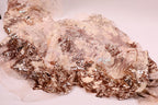 a close-up view of a fabric with a metallic, glittery texture. The fabric appears to be a blend of white and gold colors, with a metallic sheen that adds a touch of sparkle to the overall appearance. The fabric is spread out on a white surface, creating a visually striking contrast with the background.