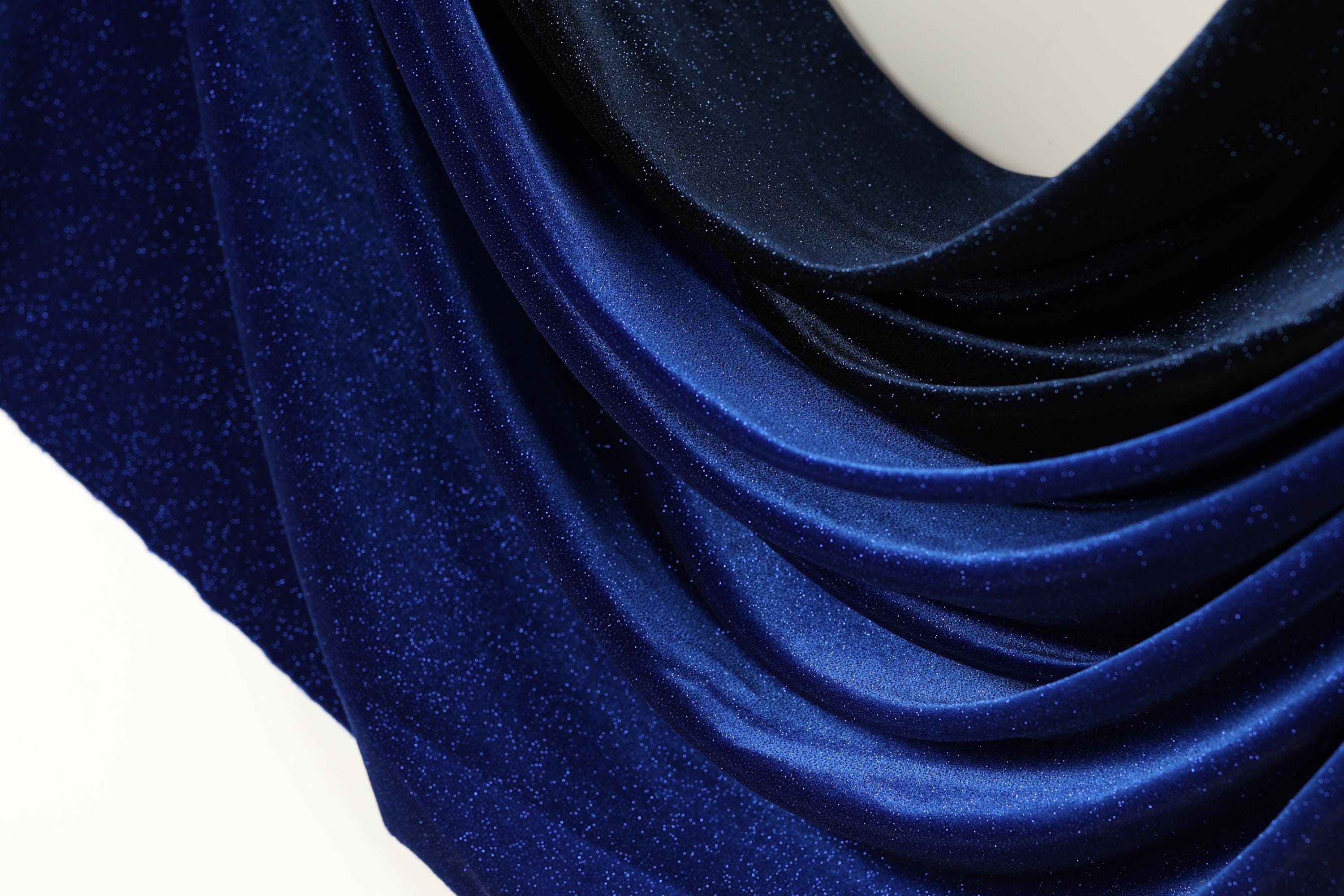 a close-up view of a blue fabric with a shiny, glittery texture. The fabric appears to be made of a shiny, metallic material, giving it a luxurious and elegant appearance.