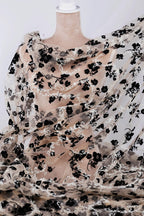a mannequin wearing a sheer, floral-patterned fabric draped over its body. The fabric has a black and white floral design, creating a visually striking contrast.