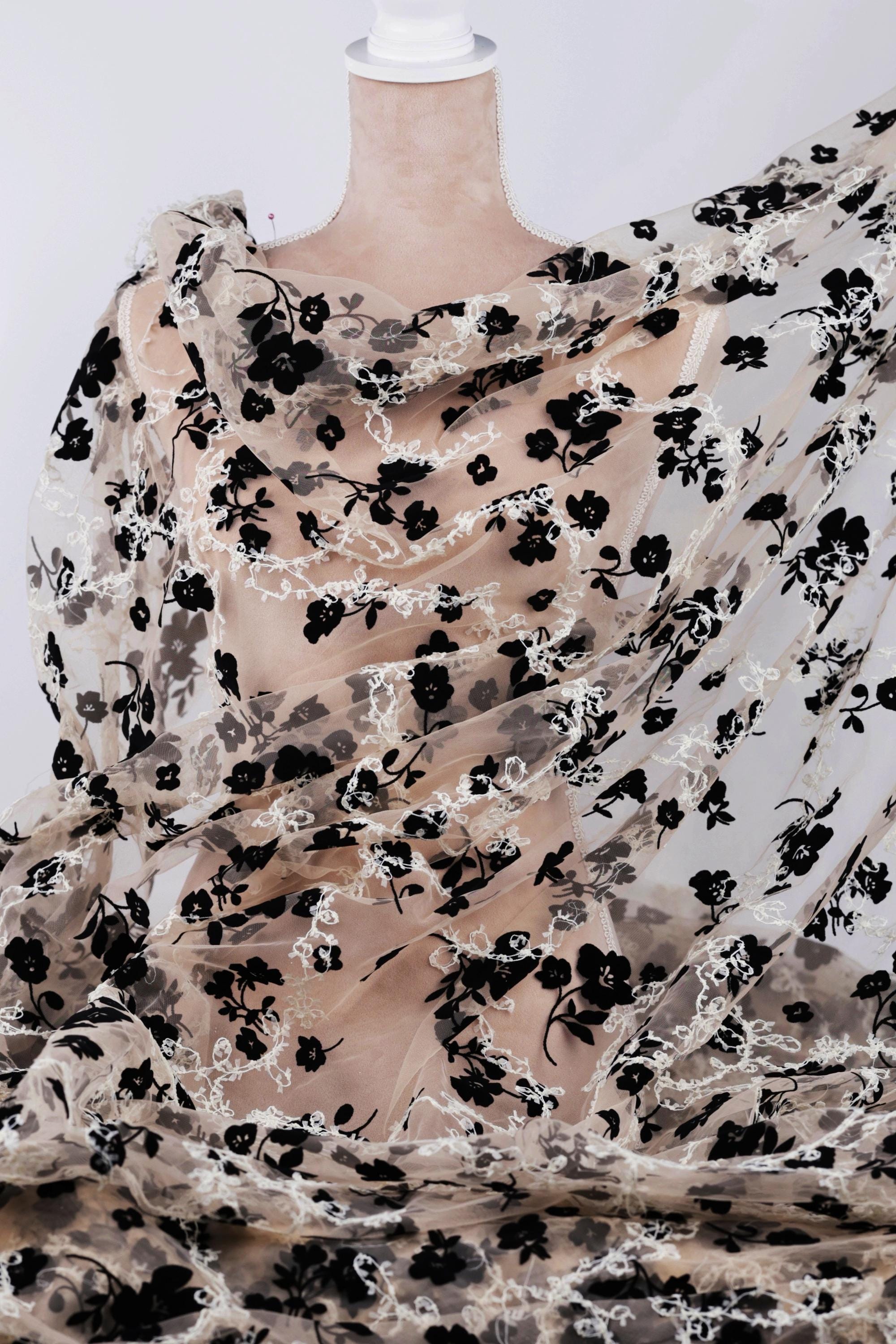 a mannequin wearing a sheer, floral-patterned fabric draped over its body. The fabric has a black and white floral design, creating a visually striking contrast.