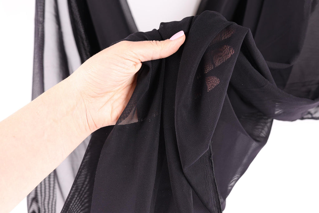 A hand is holding a black fabric with a patterned design, against a white background.